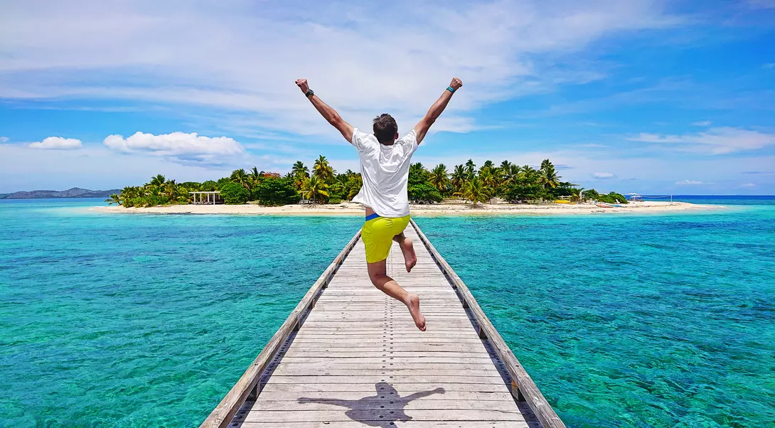 A young traveller jumping with joy on the pier on Mala Mala Island, Fiji.