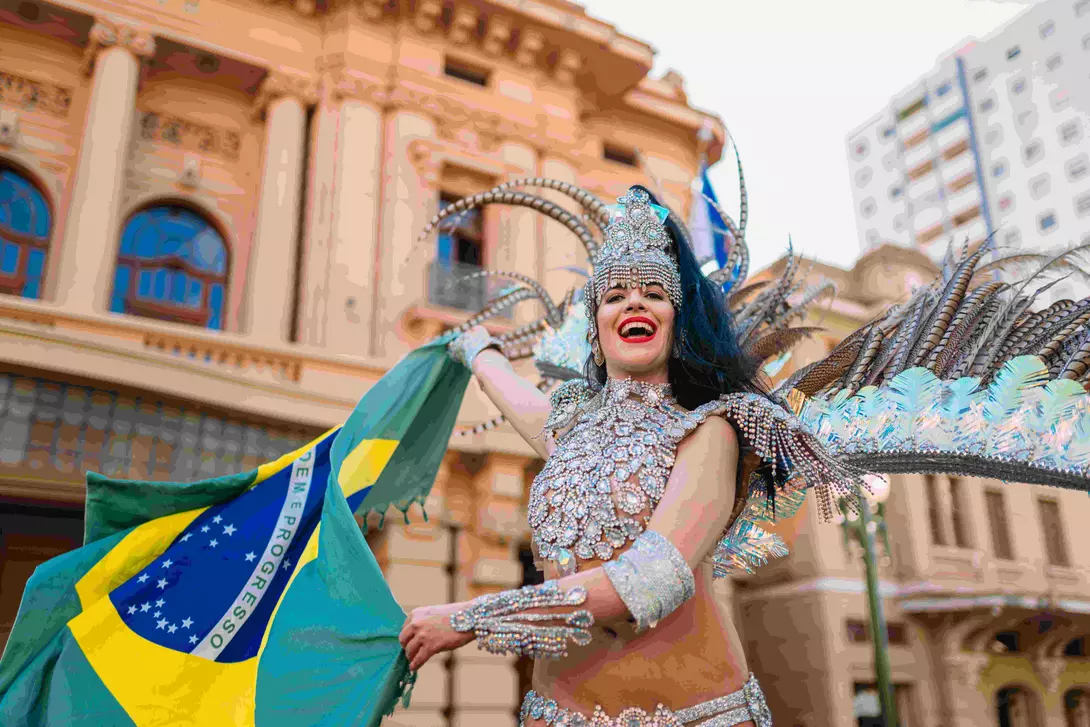 Beautiful Brazilian woman wearing colorful Carnival costume and Brazil flag during Carnaval street parade in city.