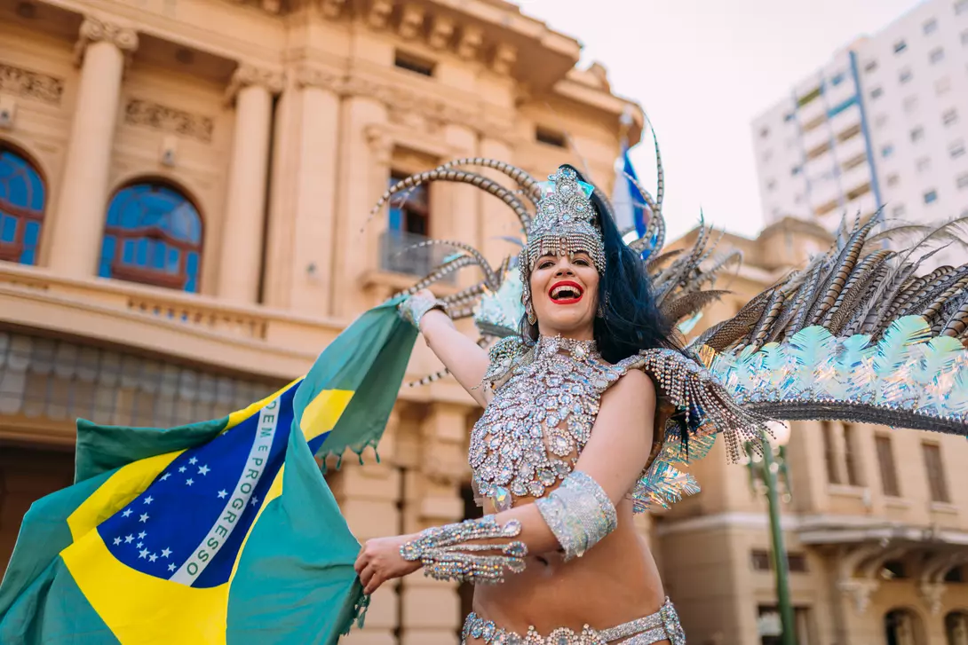 Beautiful Brazilian woman wearing colorful Carnival costume and Brazil flag during Carnaval street parade in city.