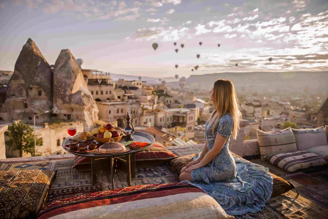 A woman sits on a rooftop in Cappadocia in the early morning sunrise in Turkey