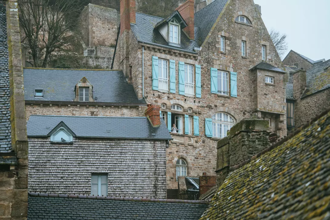 Tourist taking photos from hotel window on Mont-Saint Michel on a rainy day.