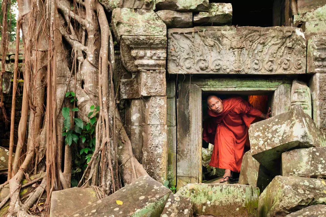 Cambodian monk ducks under a short doorway to explore an ancient temple