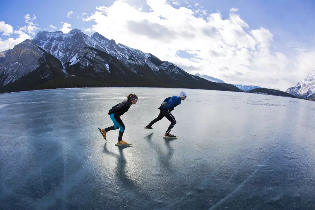 A man leads a woman on a winter speed skating adventure on Lake Minnewanka in Banff National Park