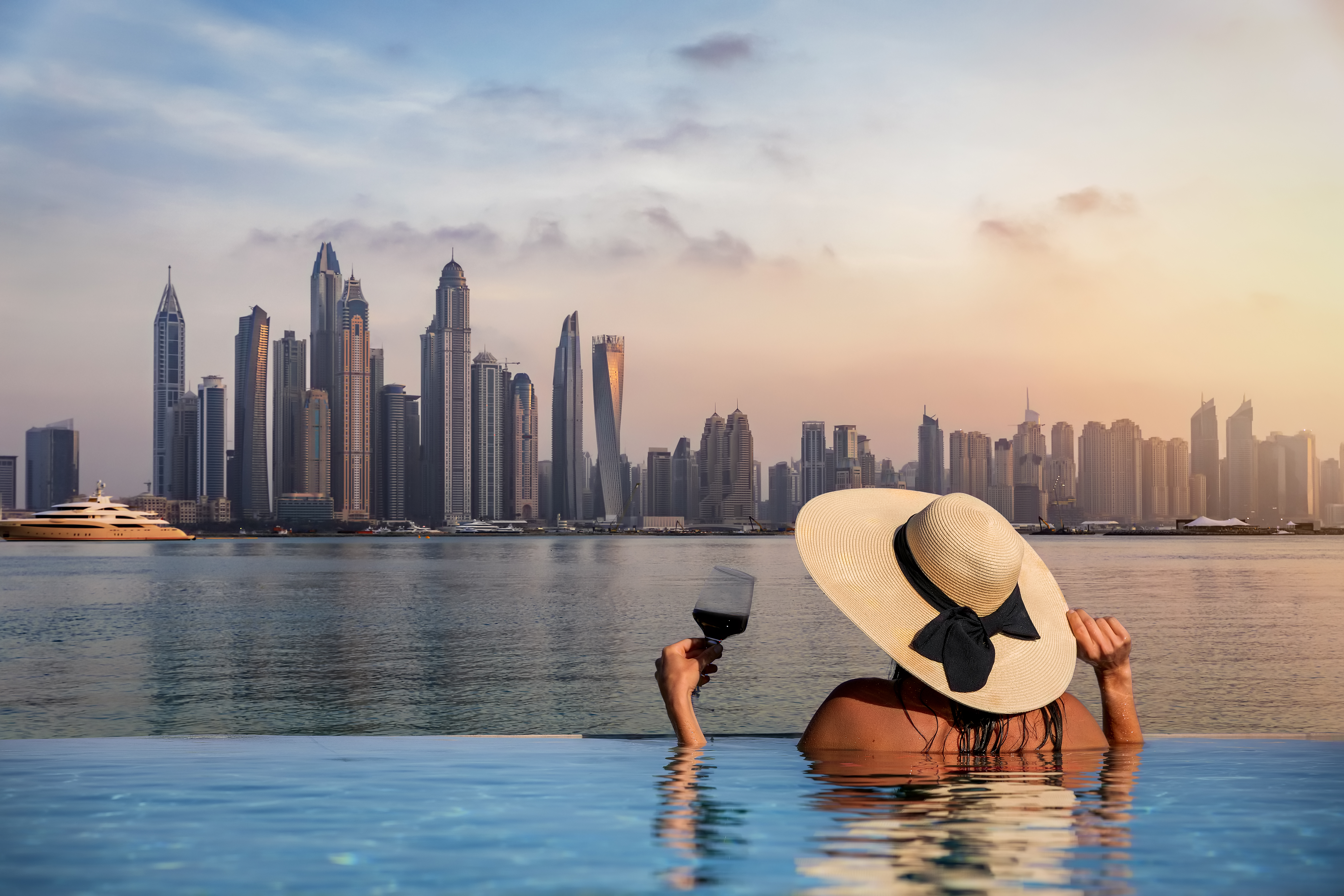 Woman at edge of a infinity pool and enjoys the view to the skyline of the Dubai Marina during sunset, UAE
