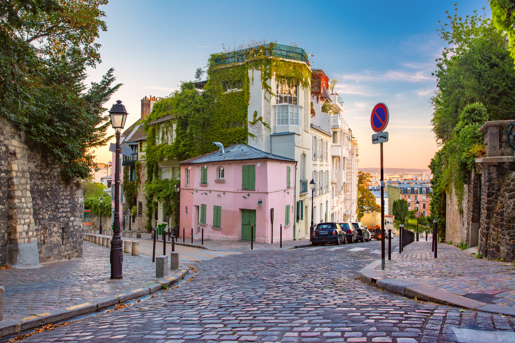 A charming cobblestone street in a picturesque neighborhood with lush greenery and pastel-colored buildings.