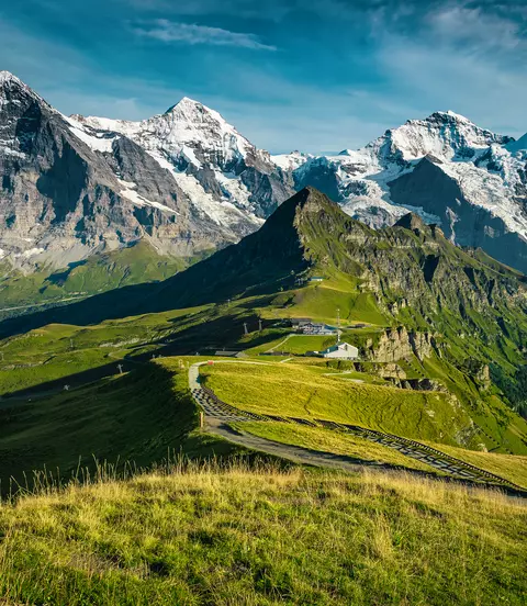 Picturesque snowy mountain ridges and deep valleys with green fields.
